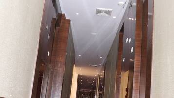 A modern hotel corridor with a wooden floor, large glass doors, and a high ceiling with recessed lighting.