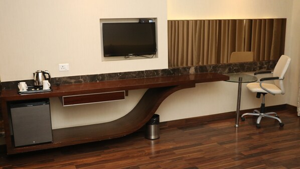 A modern hotel room with a long wooden desk, a television mounted on the wall, a small round table, and a chair.