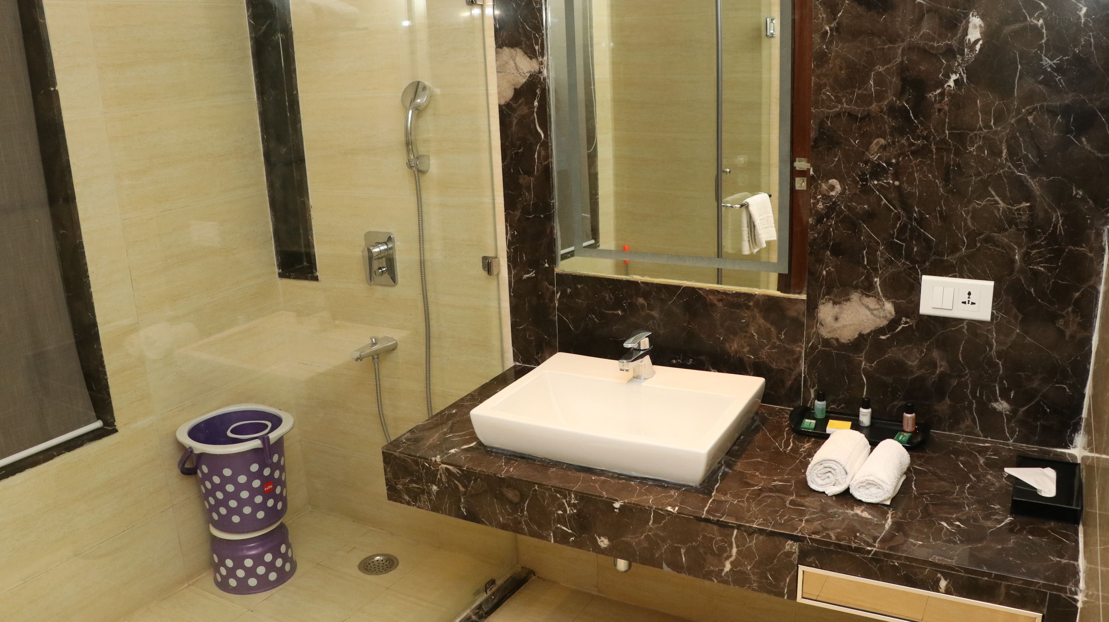 A bathroom with a marble sink, a glass shower enclosure, and a toilet with a purple polka dot trash can.