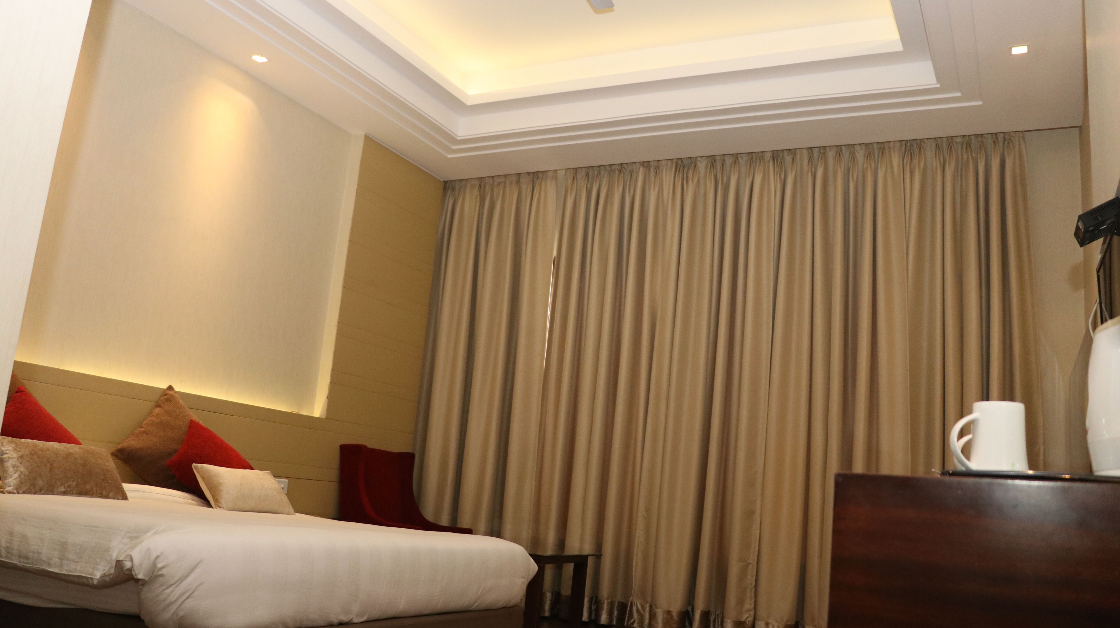 A hotel room with a bed, a nightstand, a coffee maker, and a large window with curtains.