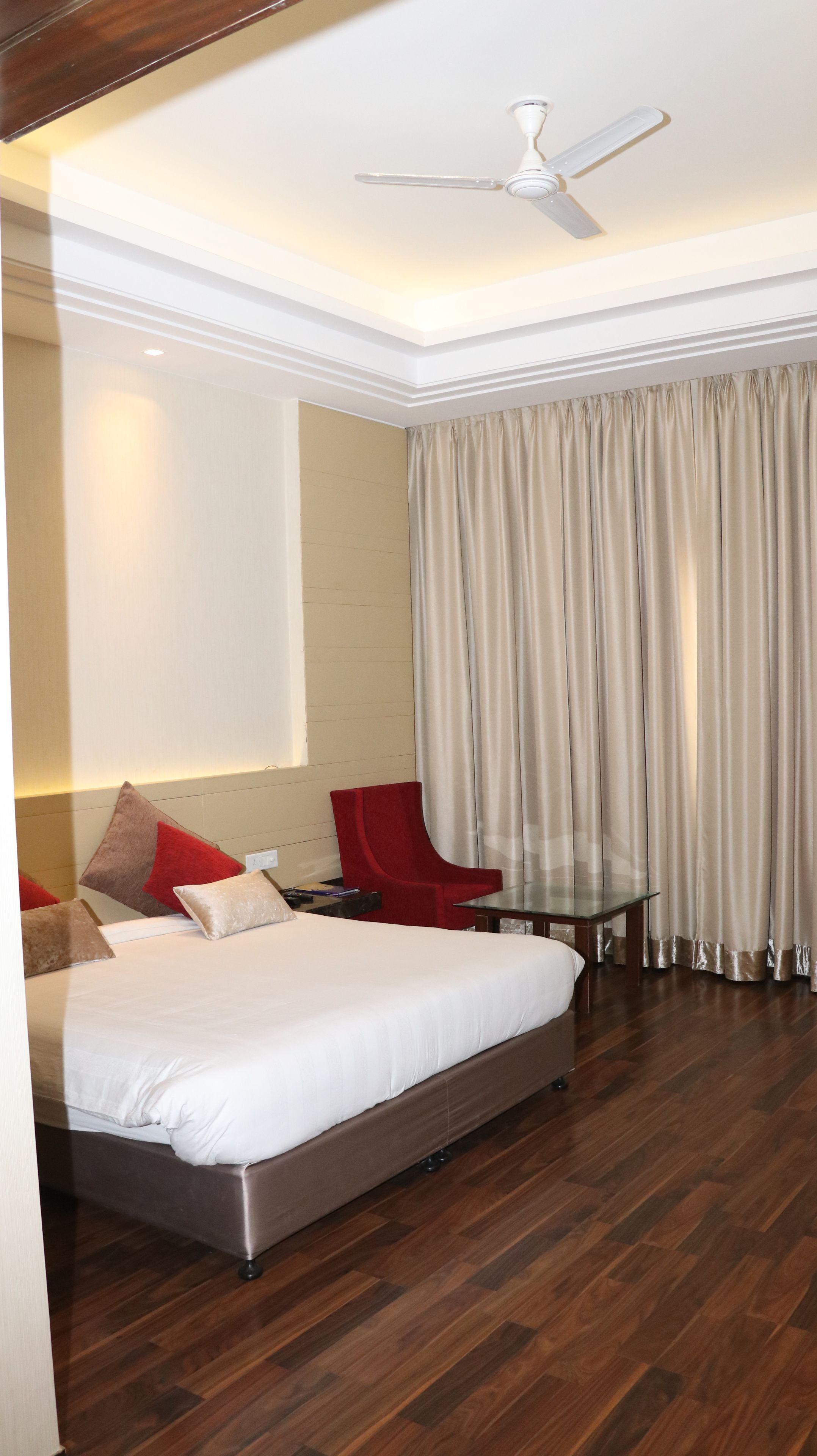 A hotel room with a bed, a red chair, a small table, and a ceiling fan.