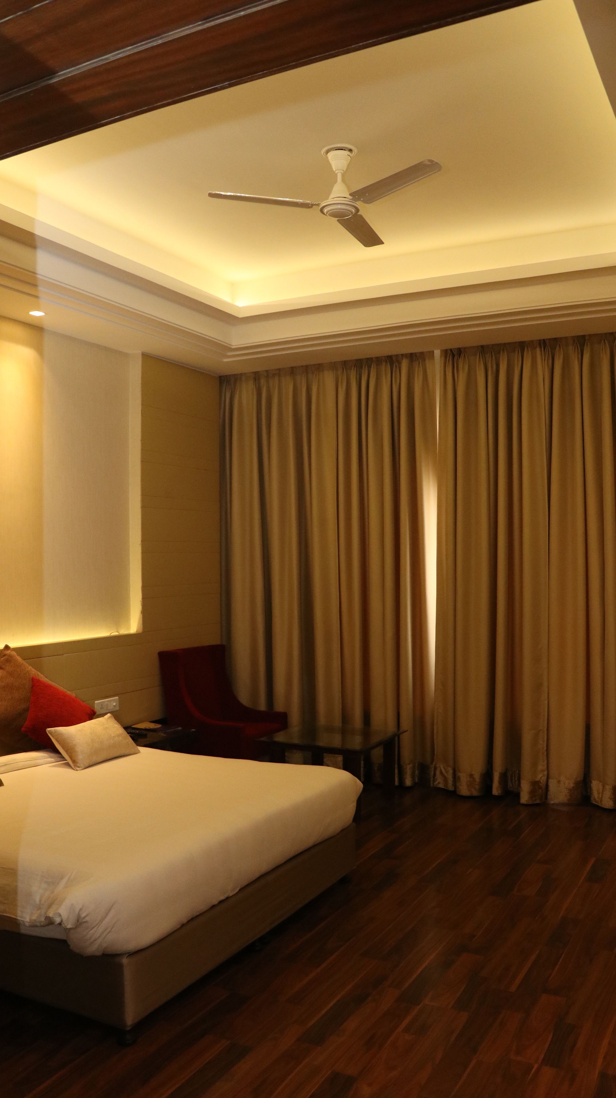 A hotel room with a bed, a ceiling fan, a red chair, and a window with curtains.