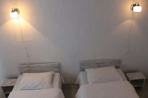 Duas camas de solteiro com cabeceiras de madeira, um criado-mudo em cada lado, e uma luminária fixada na parede entre elas.