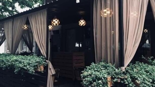 An outdoor seating area with tables and chairs, covered by curtains, and surrounded by potted plants. - Hotel Lim (Batumi)