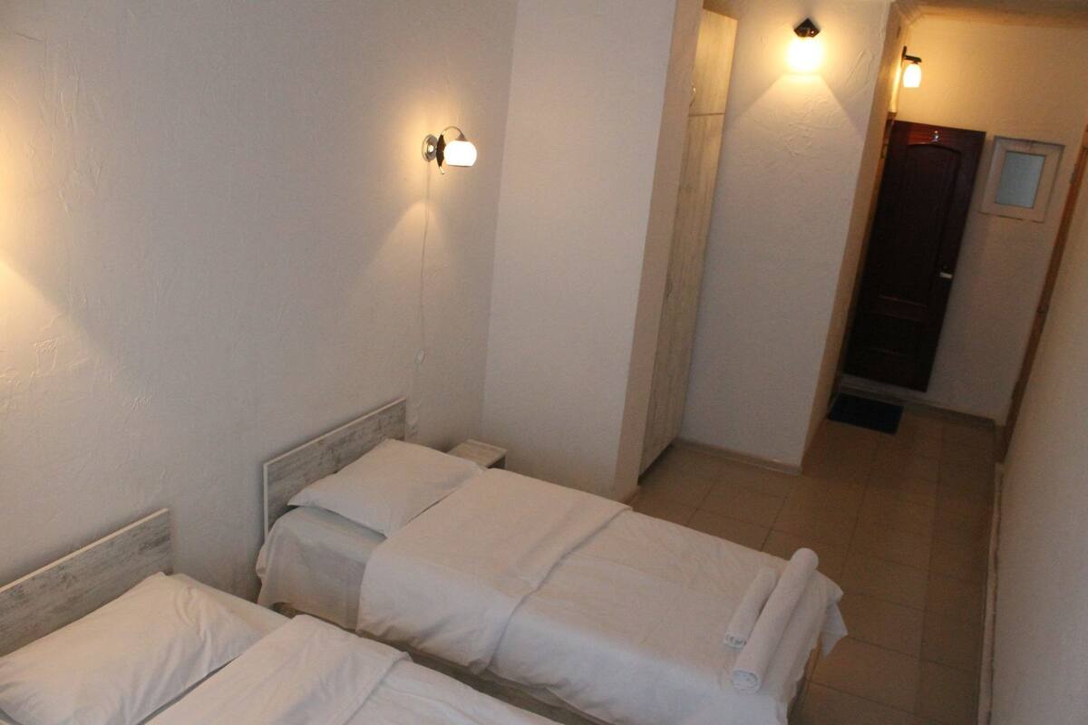 A hotel room with two beds, a nightstand, and a wall-mounted light fixture.