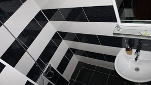 A bathroom with black and white checkered tiles, a white sink, and a glass shelf with toiletries. - Hotel Lim (Batumi)