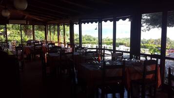 Un comedor interior con mesas y sillas, amplias ventanas con vistas a zonas verdes y colinas.
