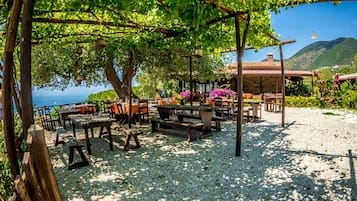 Un área de estar al aire libre con mesas y sillas, rodeada de árboles y vista al mar.