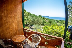 Ein Holzbalkon mit Korbstühlen und einem kleinen Tisch, mit Blick auf eine üppige grüne Landschaft und das Meer.