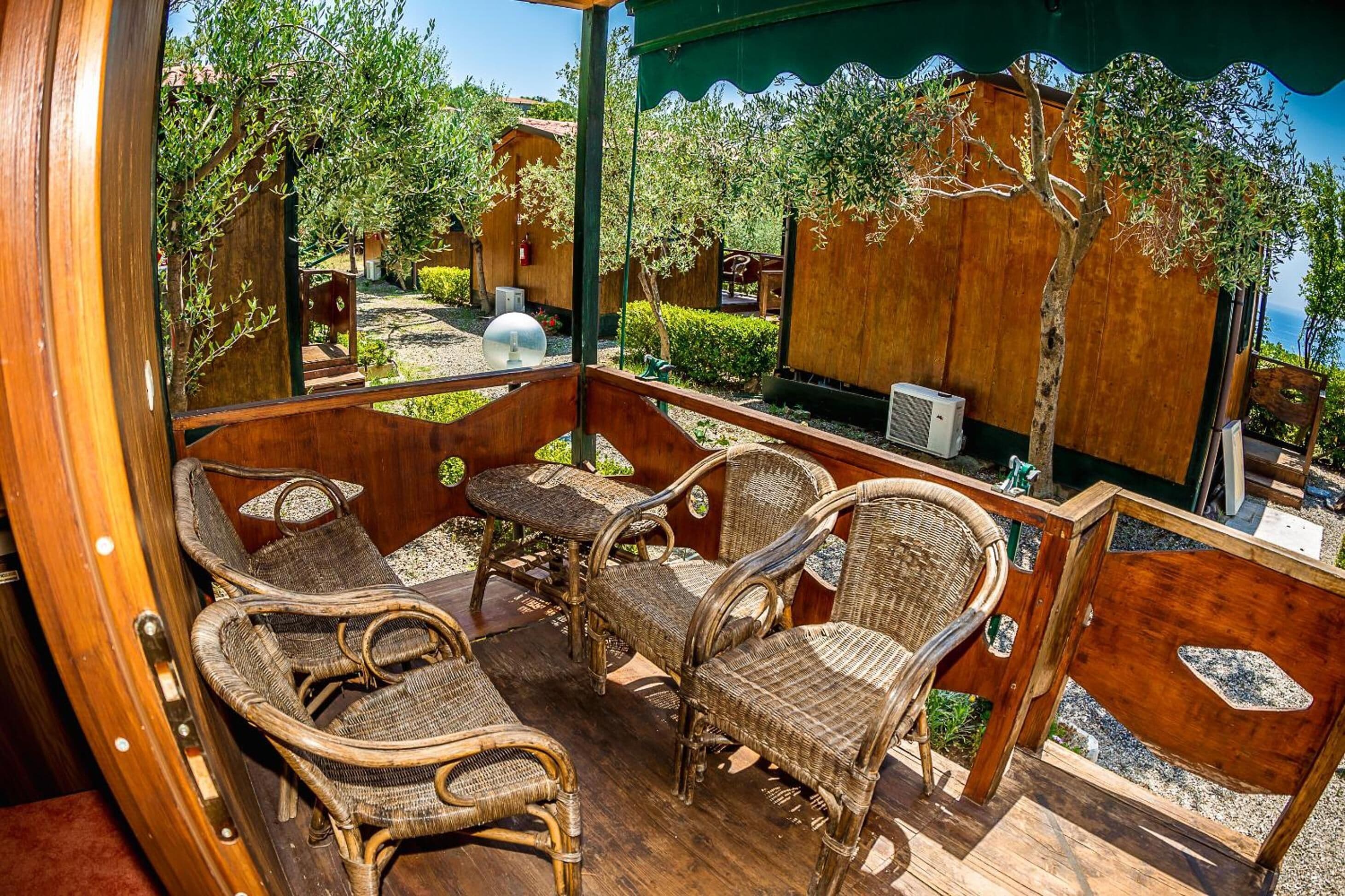 A wooden deck with wicker furniture, a round table, and a view of the sea.