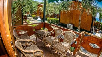 A wooden deck with wicker furniture, a round table, and a view of the sea.