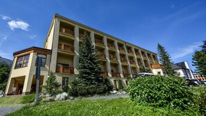 A multi-story hotel with balconies, surrounded by greenery and mountains.