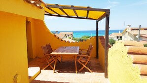 A patio with a table and chairs, overlooking a coastal view. - La Baia Apartments (San Vero Milis)
