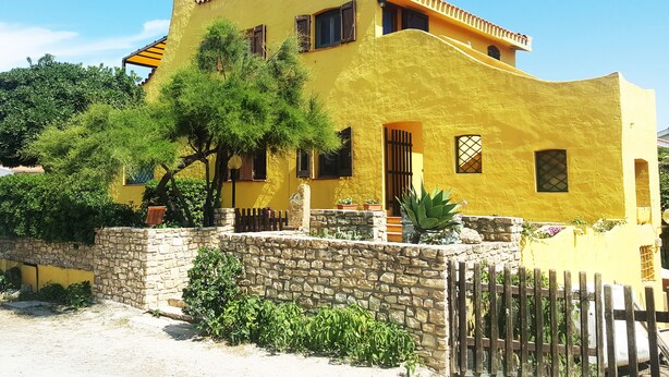 A yellow building with a stone wall and a wooden fence in front. - La Baia Apartments (San Vero Milis)