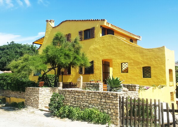 A yellow building with a stone wall and a wooden fence in front. - La Baia Apartments (San Vero Milis)
