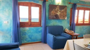 A room with a blue chair, a table with a white tablecloth, and a map on the wall. - La Baia Apartments (San Vero Milis)