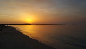 Een strand bij zonsondergang met rustig water en een heldere lucht.