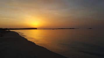 Una spiaggia al tramonto, con acque calme e cielo sereno.