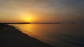 Een strand bij zonsondergang met rustig water en een heldere lucht.
