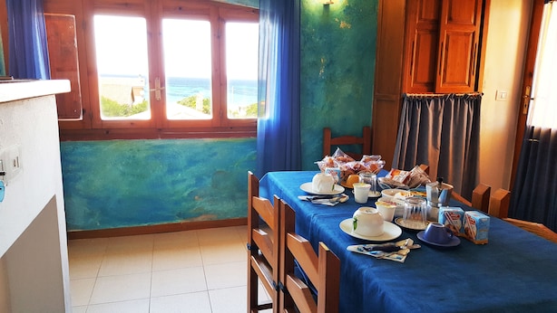 Een eethoek met een tafel gedekt voor twee personen, uitzicht op zee door grote ramen, en een blauw gordijn.