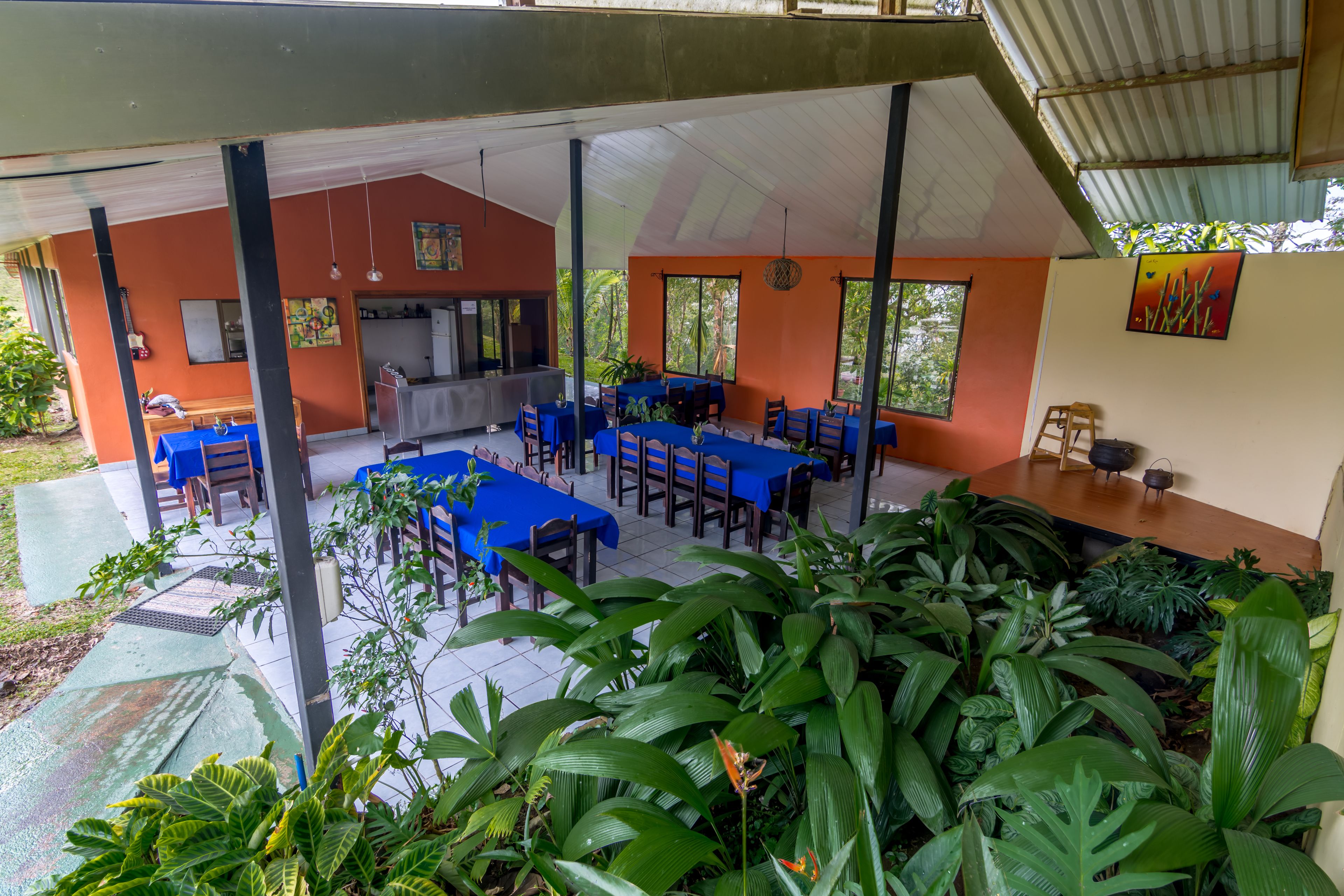 An outdoor dining area with tables and chairs, surrounded by lush greenery.