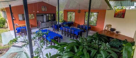 An outdoor dining area with tables and chairs, surrounded by lush greenery.