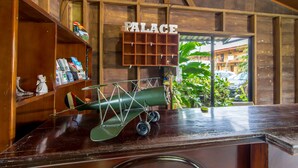 A wooden interior with a model airplane on a counter, a 'PALACE' sign, and a view of greenery outside. - Hotel Arenal Palace (La Fortuna)