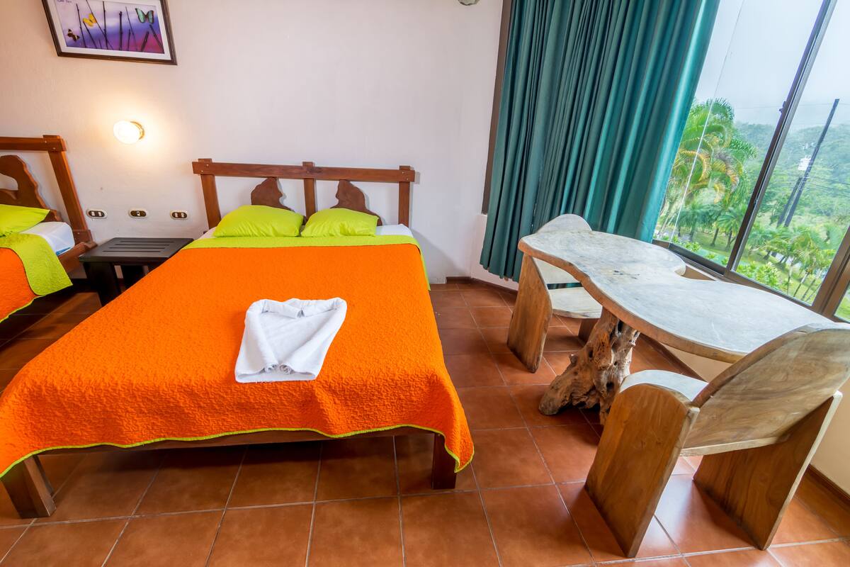 A hotel room with a large bed, a wooden nightstand, a small table, and a chair.