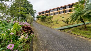 A paved pathway leading to a building with multiple windows and a sloped roof. - Hotel Arenal Palace (La Fortuna)