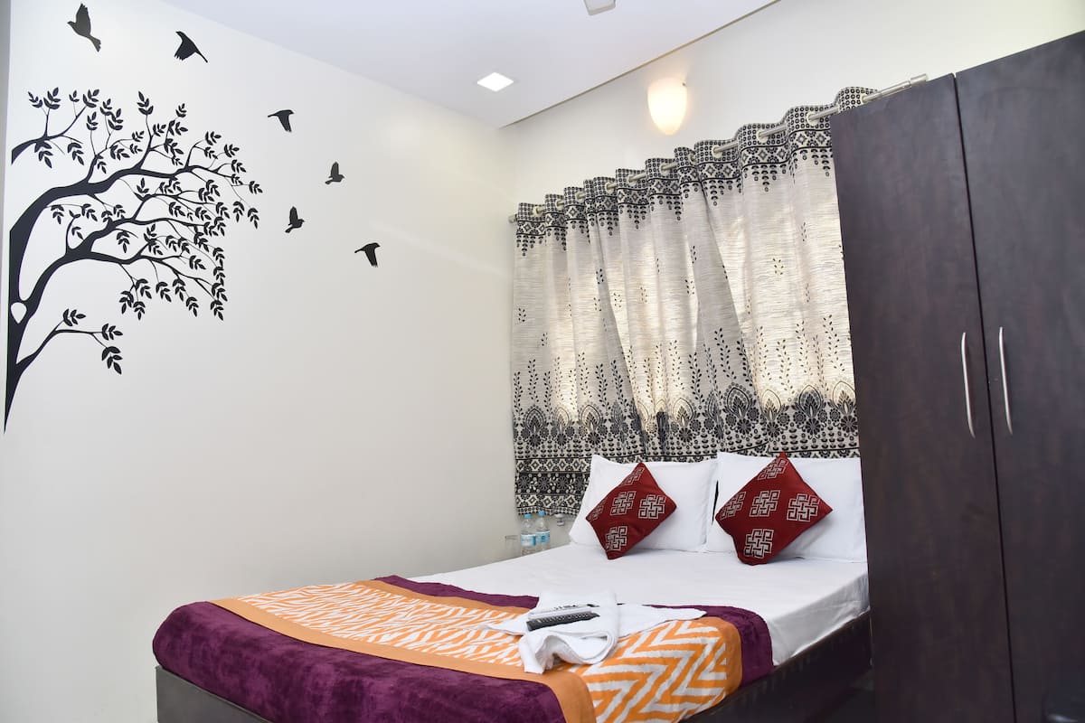 Une chambre à coucher avec un lit, une armoire, un motif d’arbre décoratif sur le mur et un rideau à motifs floraux.