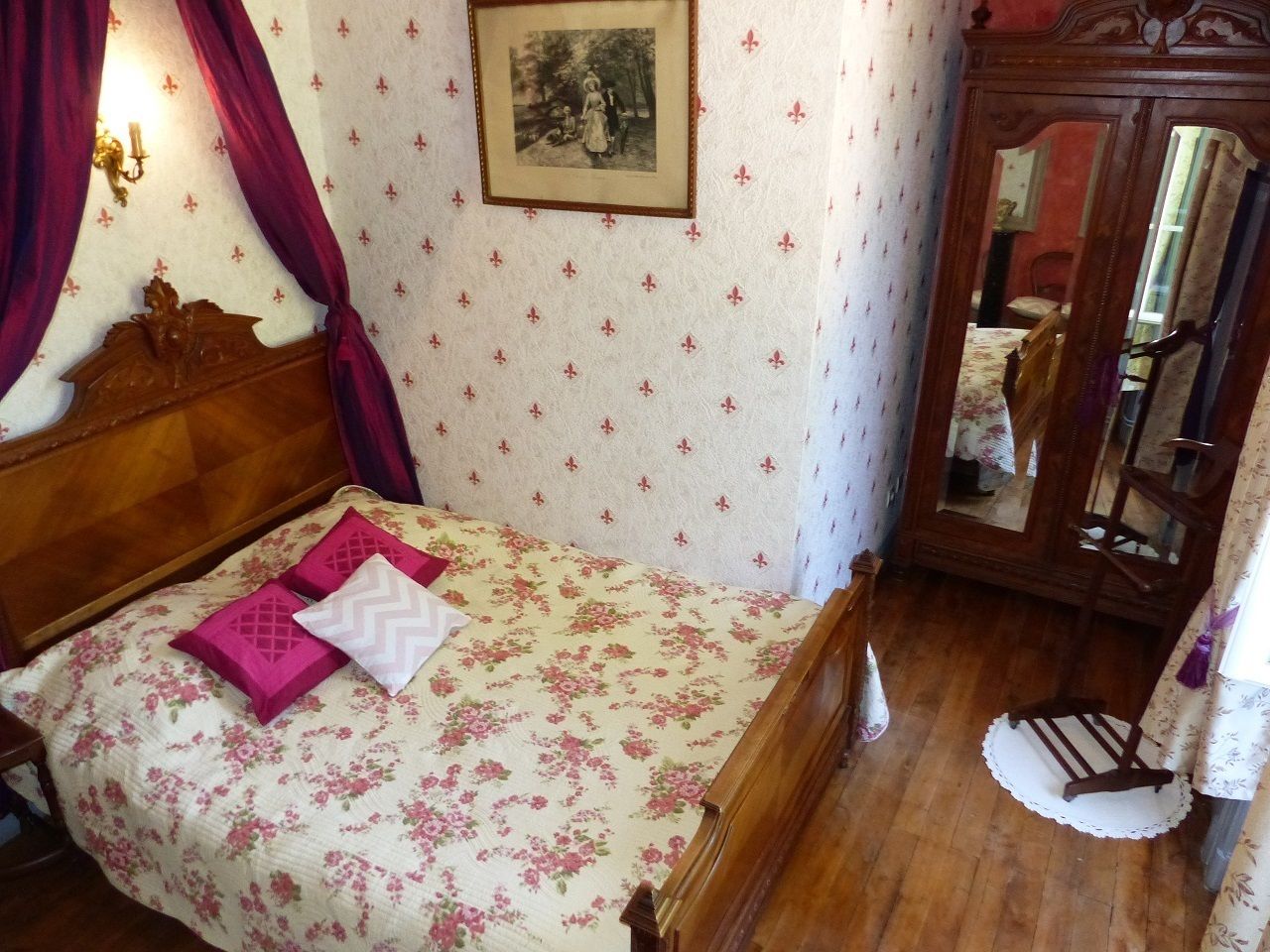 A bedroom with a wooden bed, floral bedding, a mirror, and a wall with a framed picture.