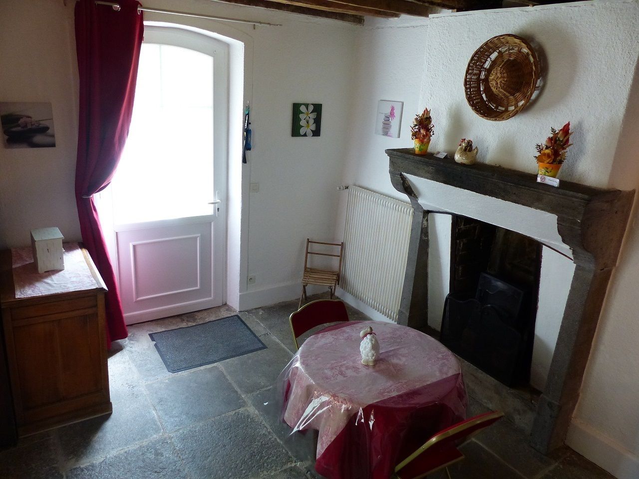 A cozy room with a fireplace, a dining table with chairs, a wooden cabinet, and a door with a red curtain.