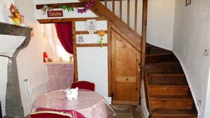 A dining area with a table covered in a transparent tablecloth, red chairs, and a wooden staircase leading to an upper level. - Château de Montsablé (Lezoux)