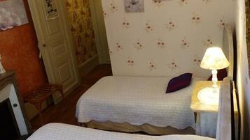 Una habitación con dos camas, una mesita de noche con una lámpara y papel tapiz con motivos florales.