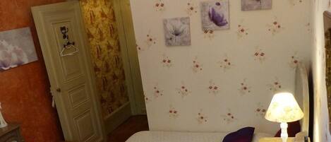 A room with two beds, a small table with a lamp, and floral wallpaper.