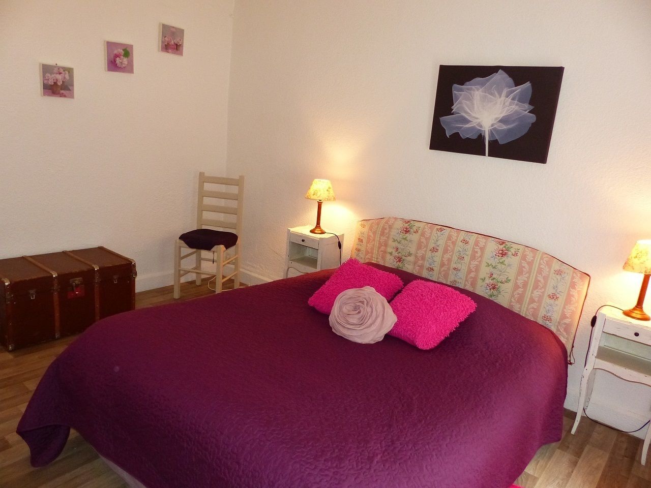Une chambre à coucher avec un grand lit, deux tables de chevet, une chaise, une valise et des éléments décoratifs sur les murs.