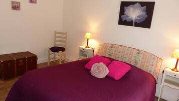 Une chambre à coucher avec un grand lit, deux tables de chevet, une chaise, une valise et des éléments décoratifs sur les murs.
