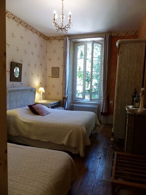 Une chambre avec deux lits, un lustre, une fenêtre avec des rideaux et un radiateur.