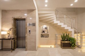 En moderne elevator med skilt for 16 personer, en trappe med gelænder, et skrivebord med lampe og en potteplante.