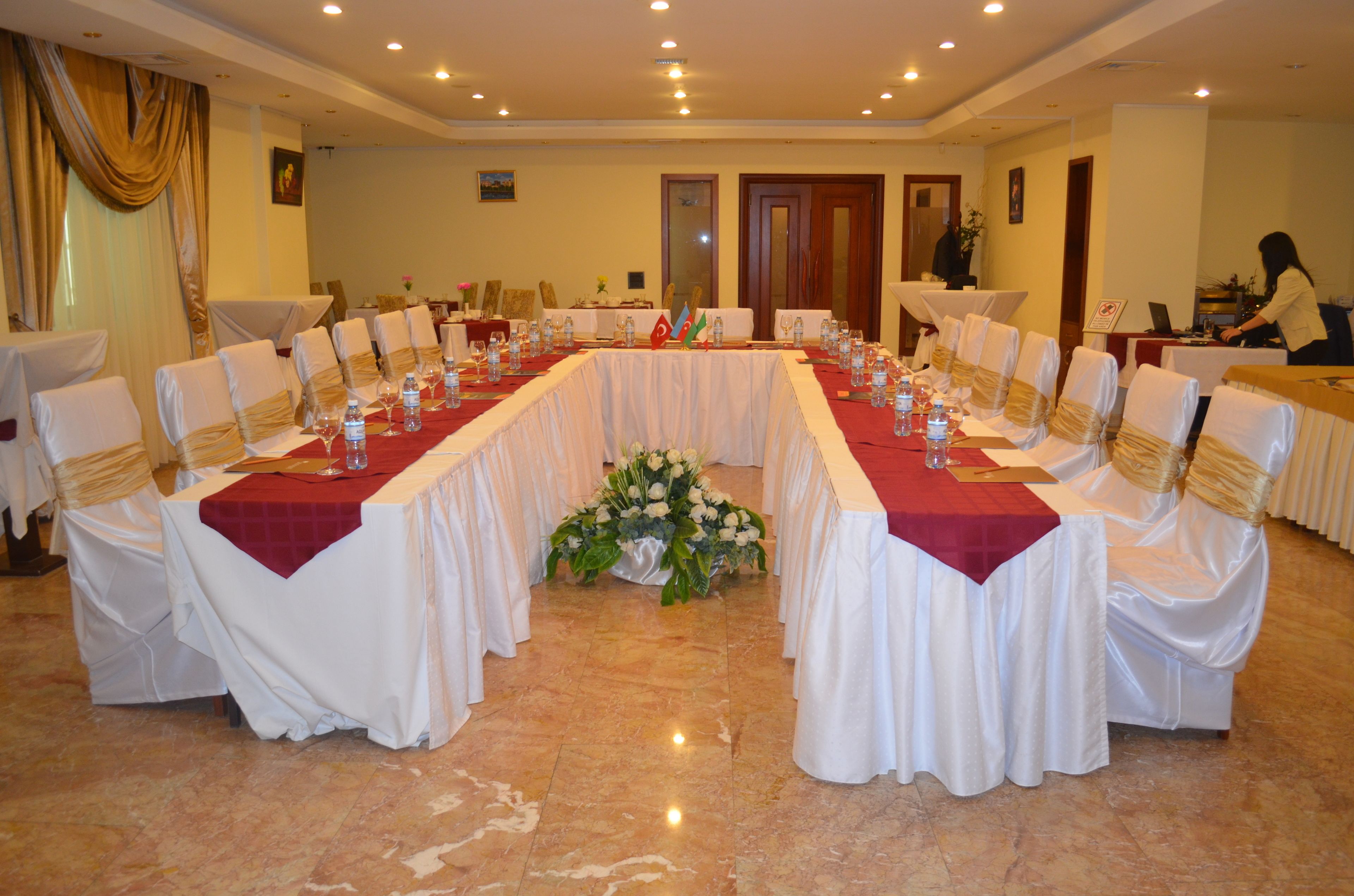 A conference room with a long table set for a meeting, surrounded by chairs with white covers and gold sashes.