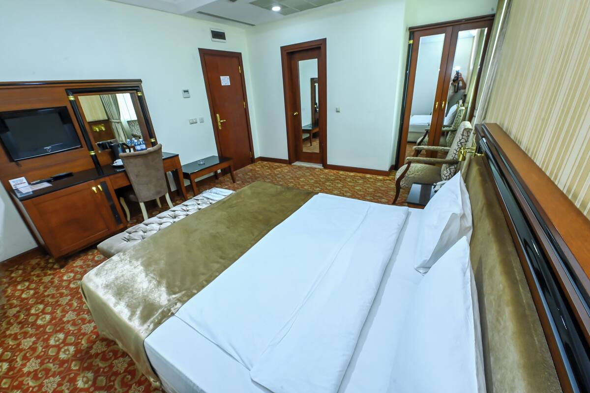 A hotel room with a bed, a desk, a chair, a TV, and a wardrobe.