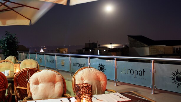 An outdoor dining area with wicker chairs and tables, a lantern, and a view of the sea at night. - Atropat Hotel Baku (Baku)