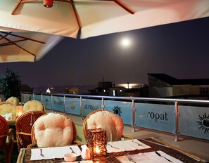 An outdoor dining area with wicker chairs and tables, a lantern, and a view of the sea at night. - Atropat Hotel Baku (Baku)