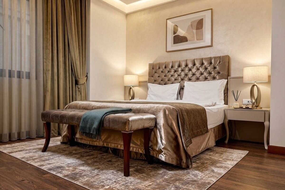 A hotel room with a large bed, a bench, two bedside tables, and a framed picture on the wall.