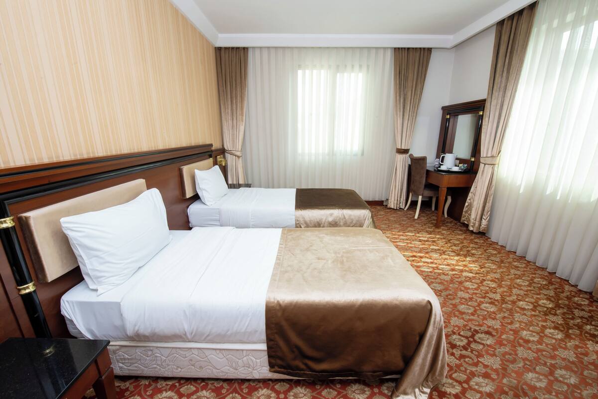 A hotel room with two beds, a desk, a chair, a mirror, and a window with curtains.