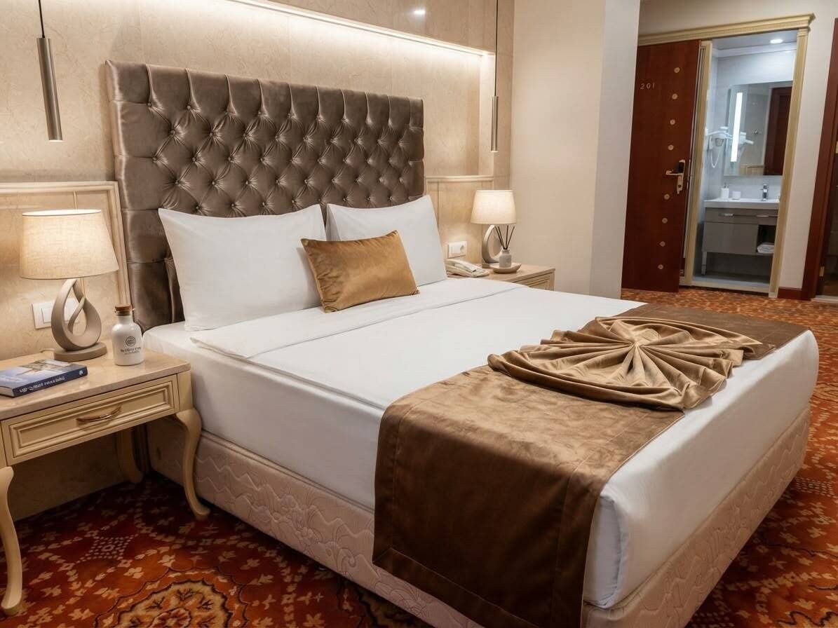 A hotel room with a large bed, two bedside tables, a nightstand, a bathroom with a mirror, and a door.