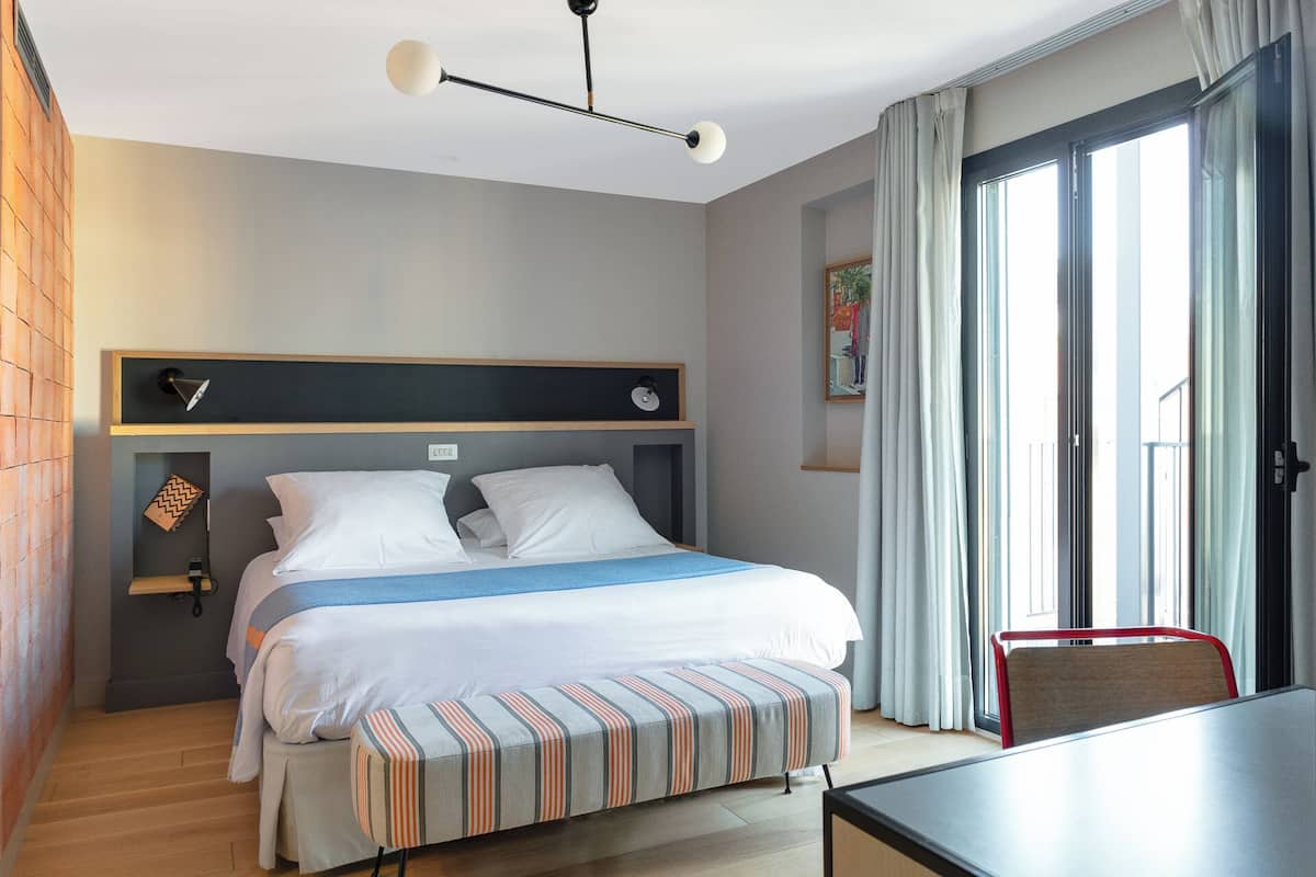 A modern hotel room with a large bed, a desk, and a view of the outdoors.
