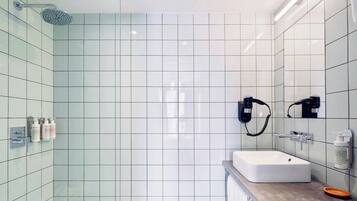Un baño moderno con ducha, lavamanos y dos secadores de pelo fijados a la pared.