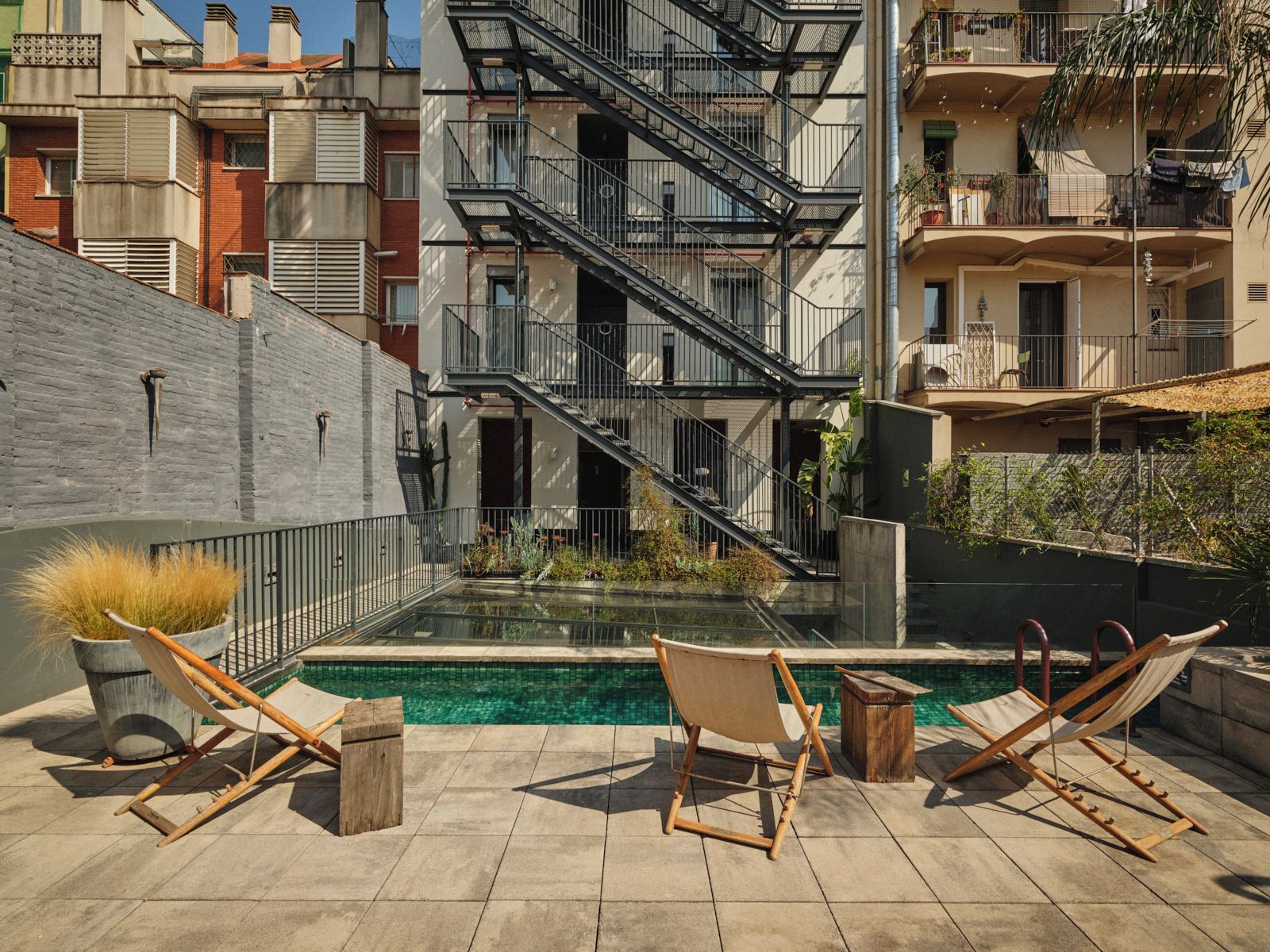 Un área de piscina en la azotea con dos sillas de descanso y una pequeña mesa, rodeada por un muro bajo y una escalera que conduce a un nivel superior.