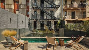 Un área de piscina en la azotea con dos sillas de descanso y una pequeña mesa, rodeada por un muro bajo y una escalera que conduce a un nivel superior.